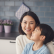 Portrait of a smiling Asian mother with her happy child looking up at her in a modern kitchen.