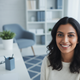 Close-up portrait of a smiling South Asian woman in a modern home office setting, conveying trust and satisfaction.